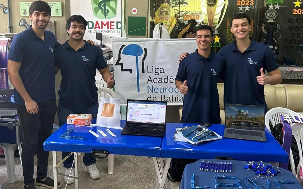 Ligantes da LANC no estande da liga, com banner e materiais sobre a mesa.